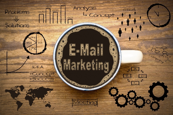 A coffee mug has the words email marketing written in coffee foam with digital graphs and symbols all over the background.