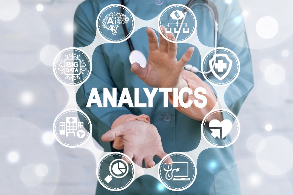 A doctor holds up his hands in front of a digital display showing the word analytics. 