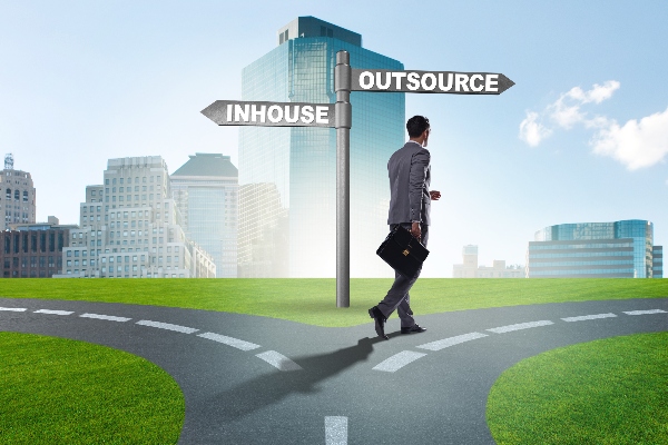 A man walks on a road that splits between one side leading to inhouse solutions and the other to outsourced solutions. He is headed toward outsourcing.