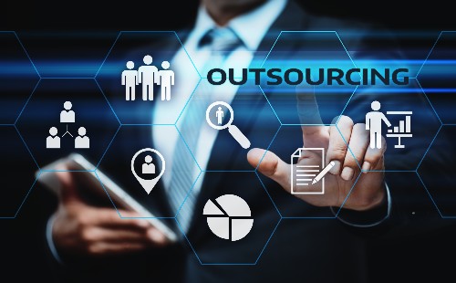 A man in a suit points to a digital display of icons and the word outsourcing