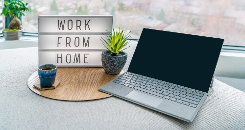 A laptop sits on a table next to a mug of coffee, a houseplant, and a sign that reads 